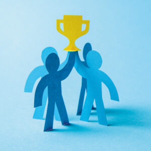 Four blue people cut out from cardboard holding award on blue background