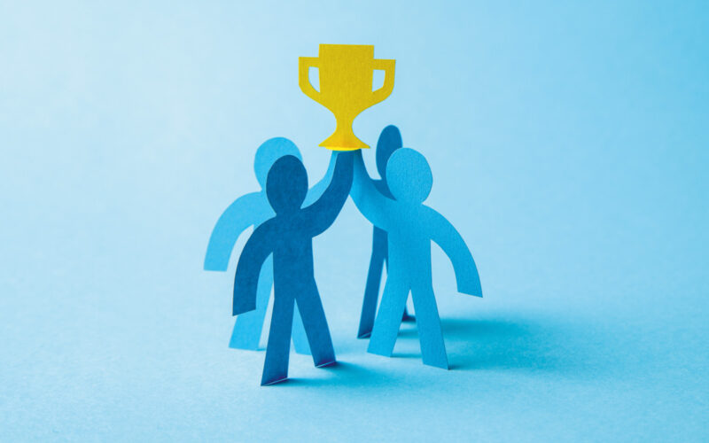 Four blue people cut out from cardboard holding award on blue background