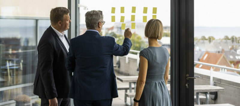 Three experts from Plougmann Vingtoft brainstorming using post-its on window
